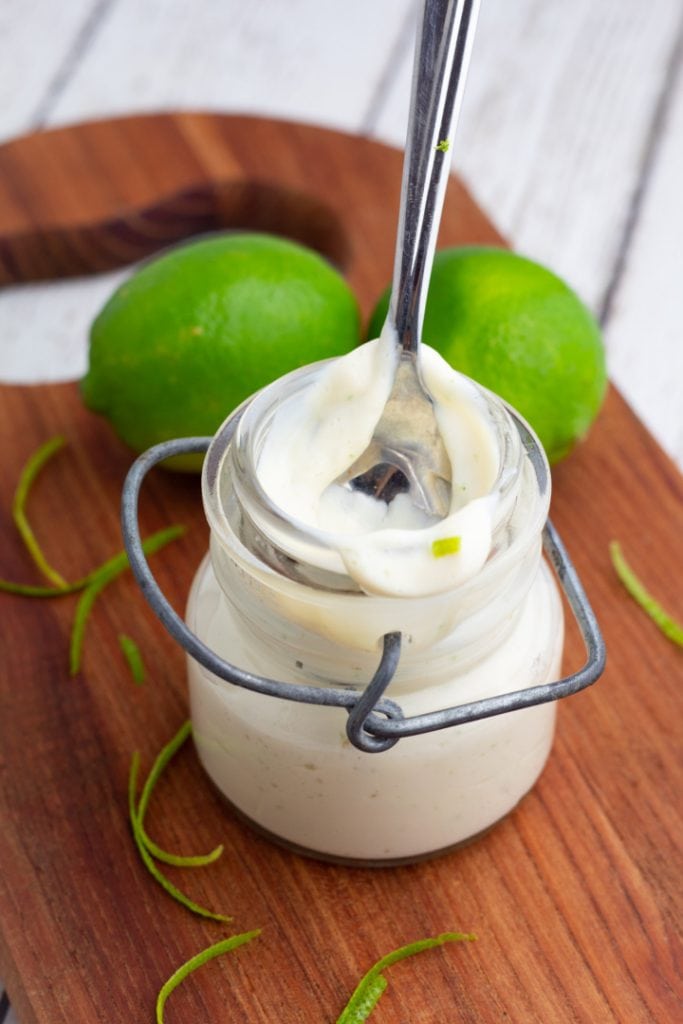 small jar with lime sauce and spoon with limes in background