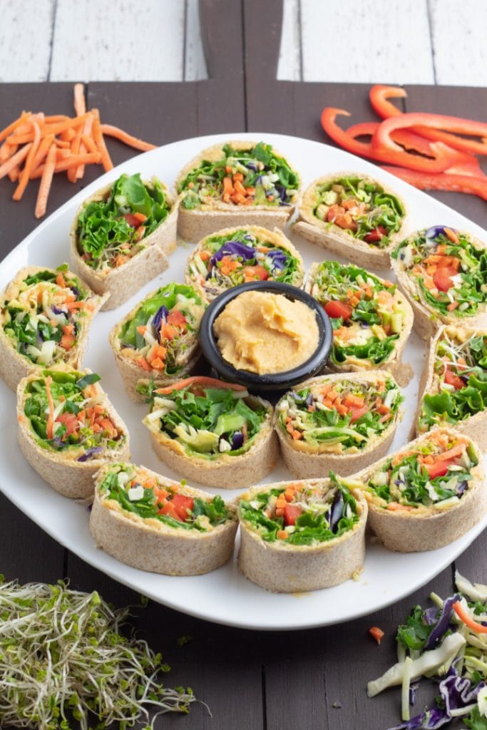 white serving tray with hummus in center and sandwich pinwheels surrounding it