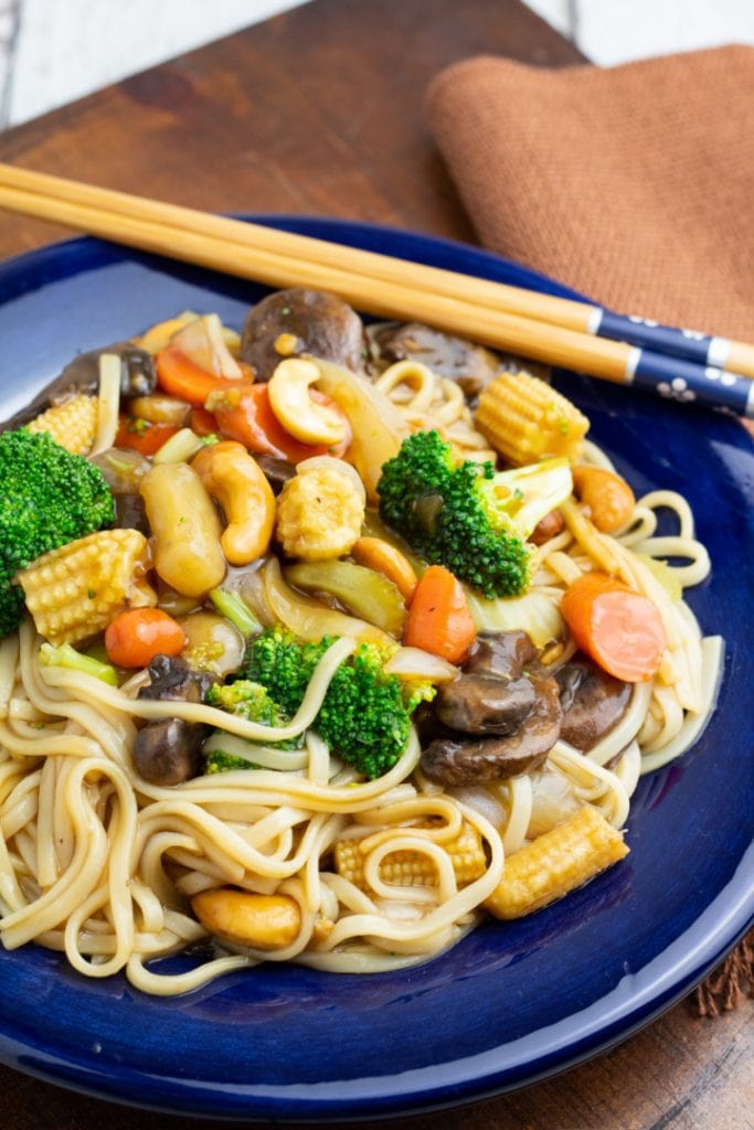 udon noodle stir fry in bright blue plate with chopsticks on side