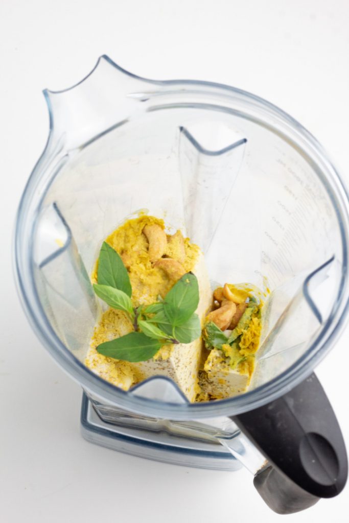 blender filled with tofu, cashews, spices, and basil