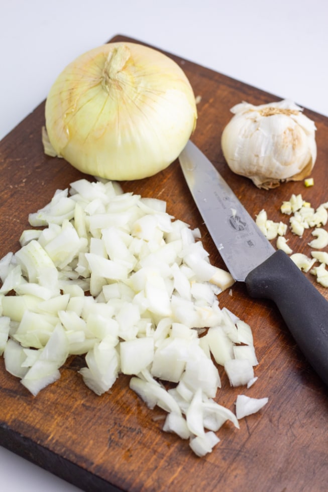 brown cutting board with diced onions and garlic and knife