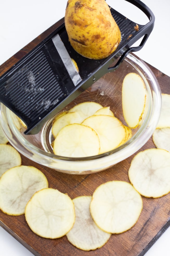 russet potatoes being sliced on mandoline over bowl