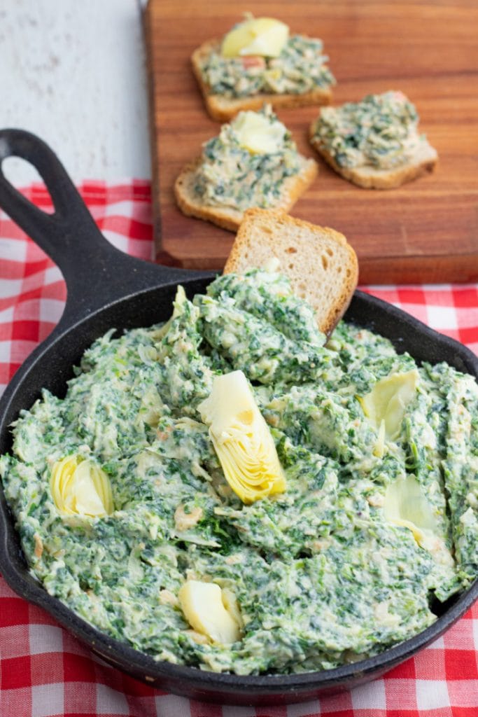 spinach dip in cast iron skillet topped with artichokes
