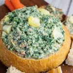 sour dough bread bowl filled with vegan spinach artichoke dip with chunks of bread surrounding