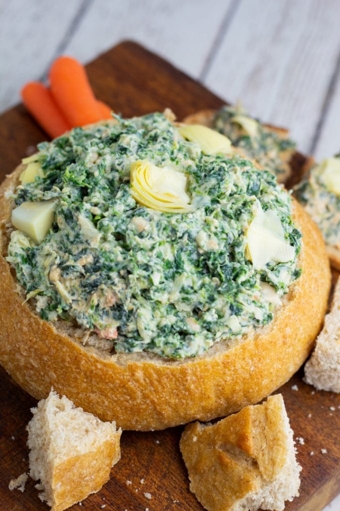 sour dough bread bowl filled with vegan spinach artichoke dip with chunks of bread surrounding