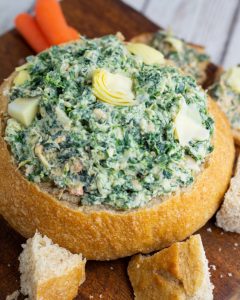 sour dough bread bowl filled with vegan spinach artichoke dip with chunks of bread surrounding