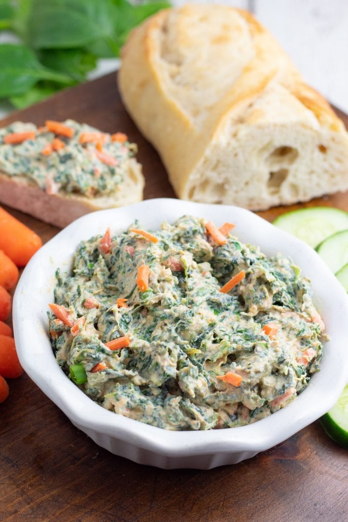 spinach dip in white bowl with crusty bread in background