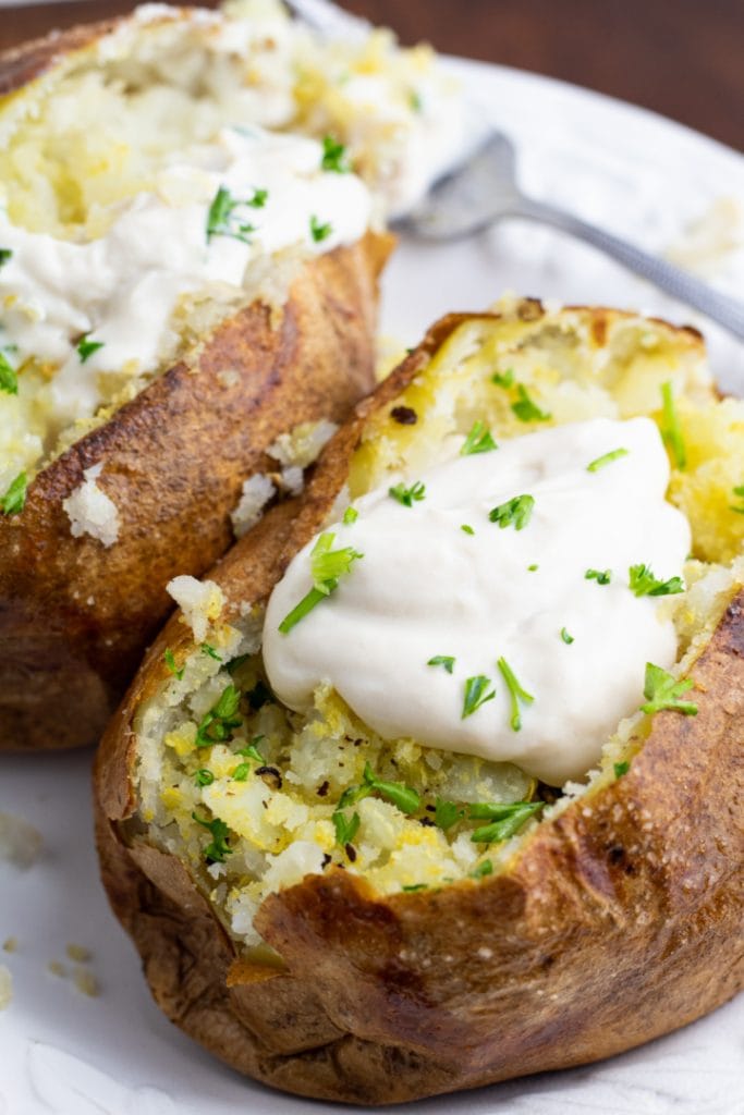 close up of two air fryed baked potatoes topped with vegan sour cream on white plate