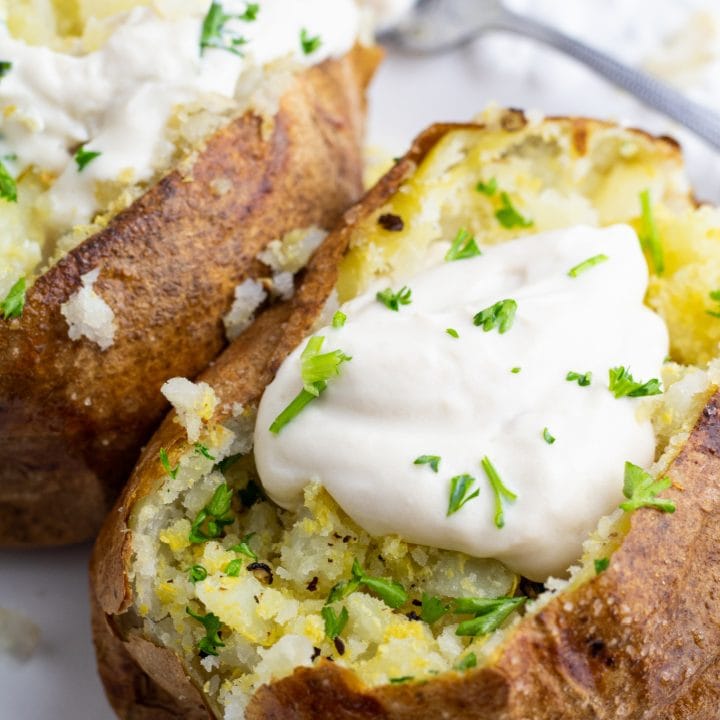 close up of two air fryed baked potatoes topped with vegan sour cream on white plate