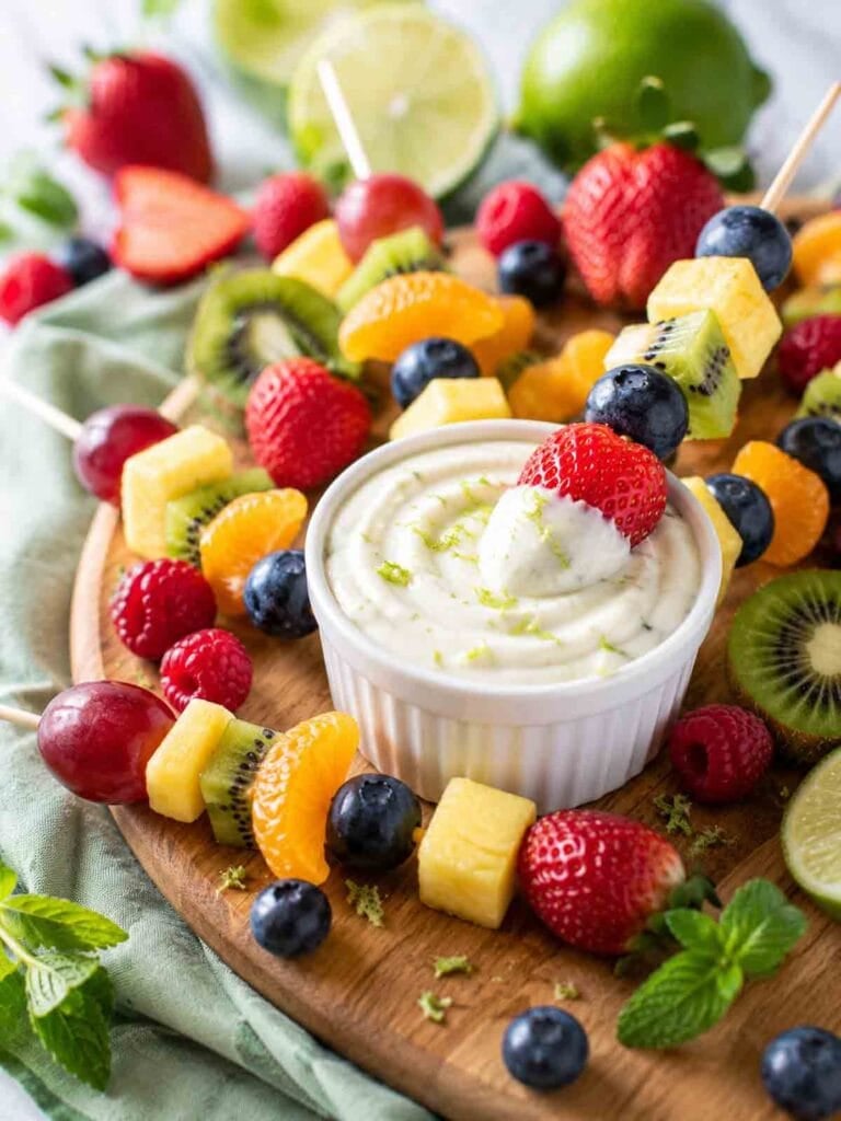colorful fruit skewers on a platter with a bowl of fruit lime sauce.