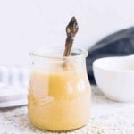 clear glass jar filled with homemade tahini sauce with a spoon inside jar.
