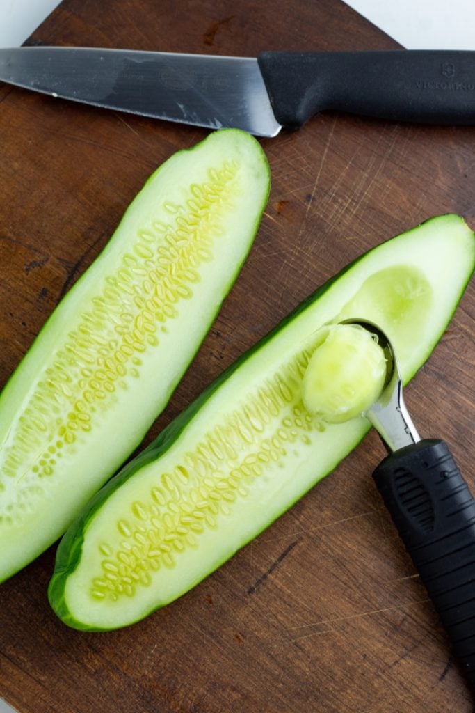 cucumbers being deseeded with spoon on cutting board