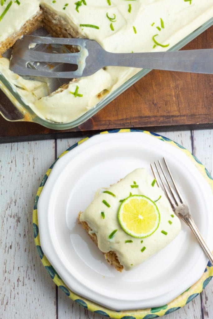 overhead shot of a slice of lime cake on white plate and baking dish with serving missing