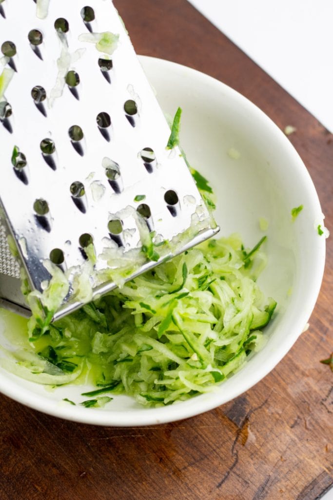 cucumber being grated into white bowl