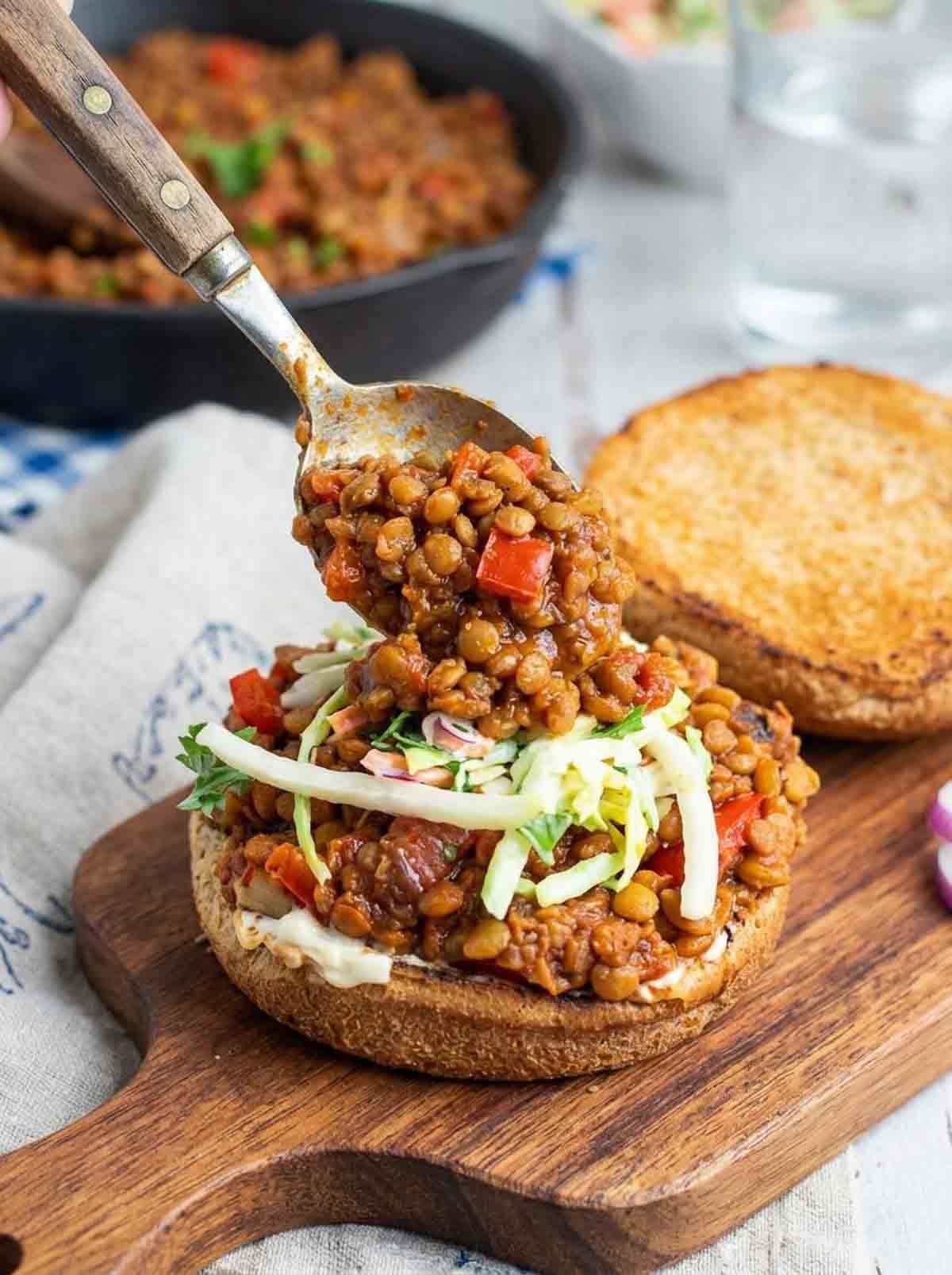 lentil sloppy joe filling being spooned onto a bun.