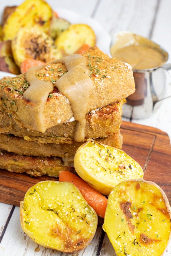 slices of baked tofu stacked up with vegan gravy dripping off and roasted potatoes in front