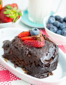 chocolate cake slice in white dish topped with strawberrie slices with glass milk and blueberries in background