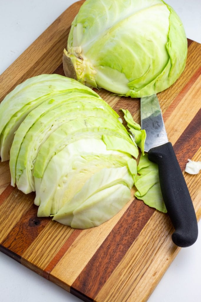 cabbage head sliced in half on cutting board with knife