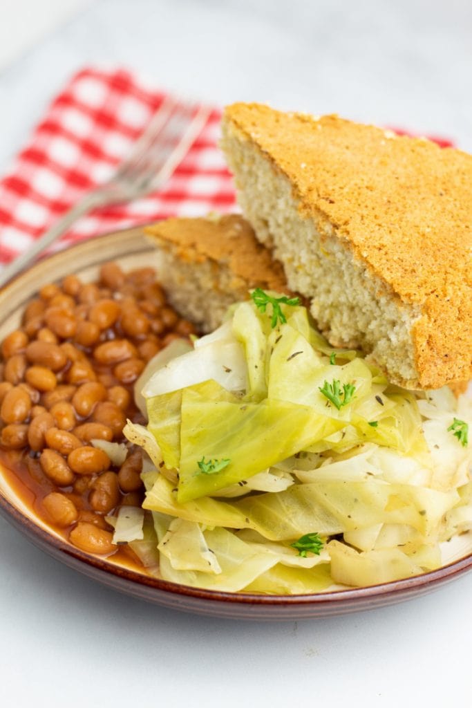 plate with cooked cabbage, baked beans, and cornbread