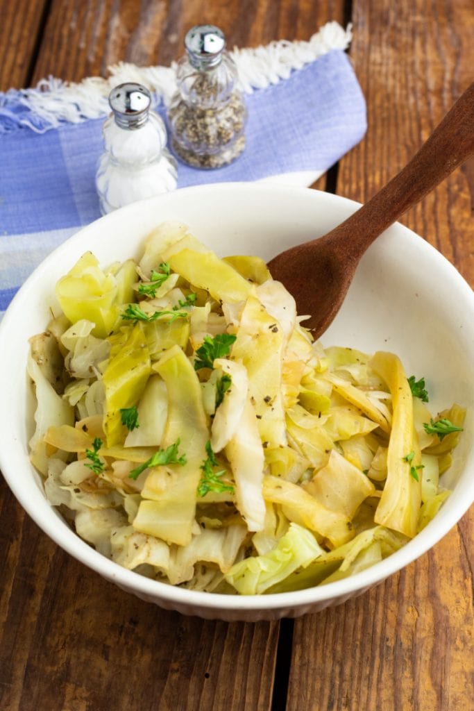 white bowl of cooked cabbage on wood table