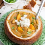 leafy green platter with bread bowl filled with vegan sweet potato soup and a spoon and bread chunks