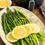 cooked asparagus with lemon slices in front of an air fryer.