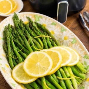 cooked asparagus with lemon slices in front of an air fryer.