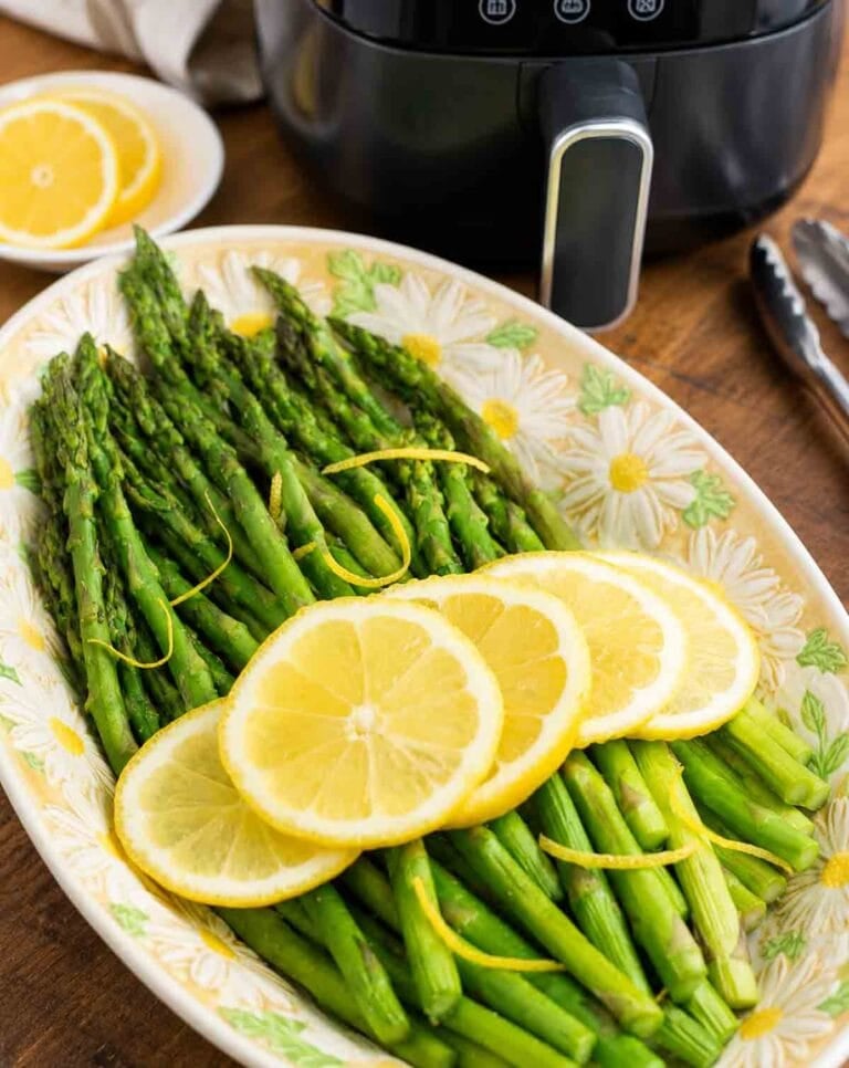 cooked asparagus with lemon slices in front of an air fryer.