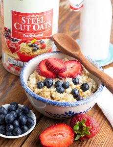 blue rimmed bowl filled with cookd steel cut oatmeal with wooden spoon on table with box of steel cut oats
