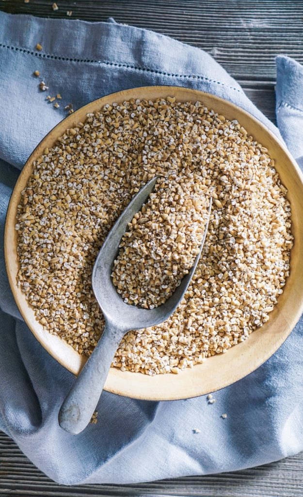 Raw Organic Steel Cut Oats in a Bowl on Wood Background.