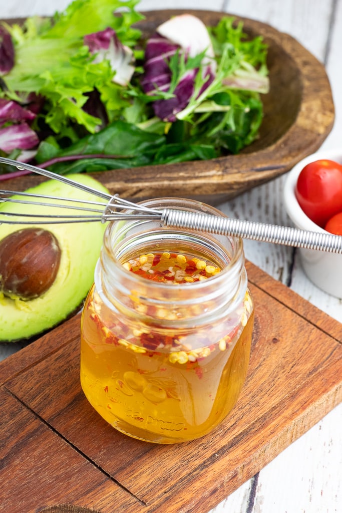 small mason jar filled with oil free vinegar sauce with whisk. avocado and salad in background