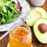 mason jar filled oil free salad dressing and whisk on top avocado in background
