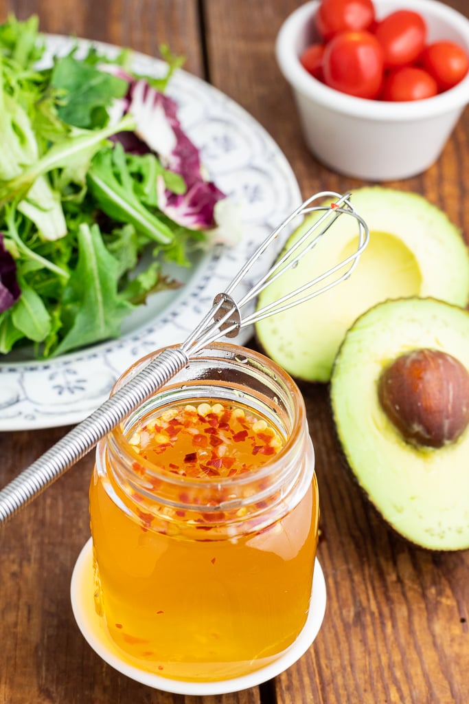 mason jar filled with oil free salad dressing and whisk on top avocado in background