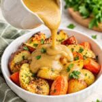 golden gravy being poured over roasted potatoes and carrots.