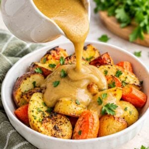 golden gravy being poured over roasted potatoes and carrots.