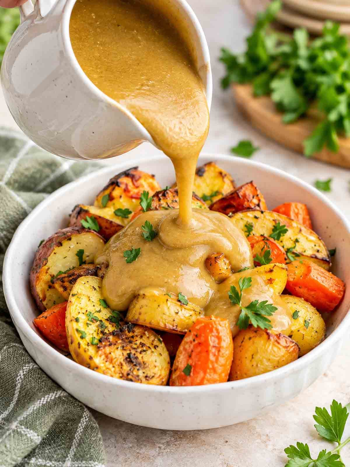 golden gravy being poured over roasted potatoes and carrots.