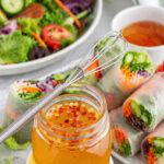 oil-free Thai vinegar sauce in a jar with garden rolls and salad in background.