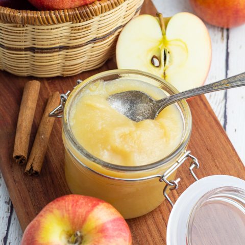 homemade unsweetened applesauce in jar with lid surrounded by red apples