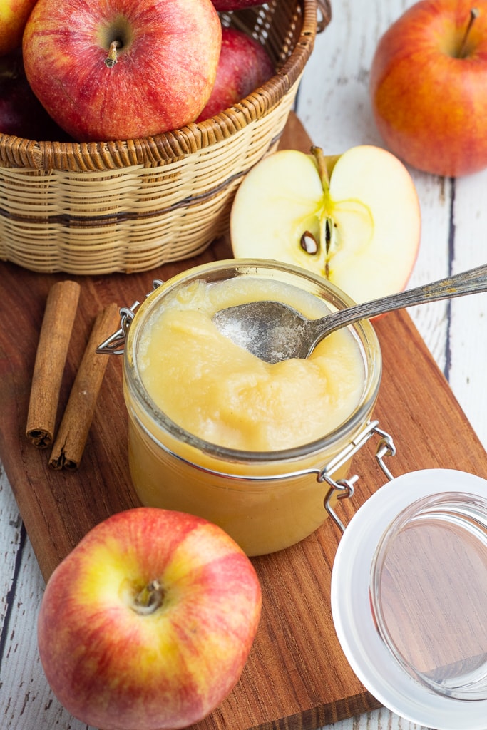 homemade unsweetened applesauce in jar with lid surrounded by red apples
