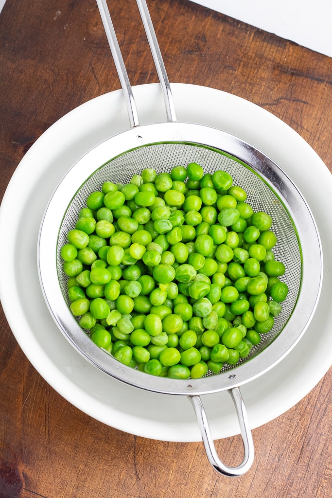 green peas in metal strainer over white bowl