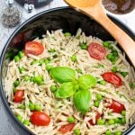 orzo pasta with tomatoes, green peas, and basil in large black bowl with wooden spoon