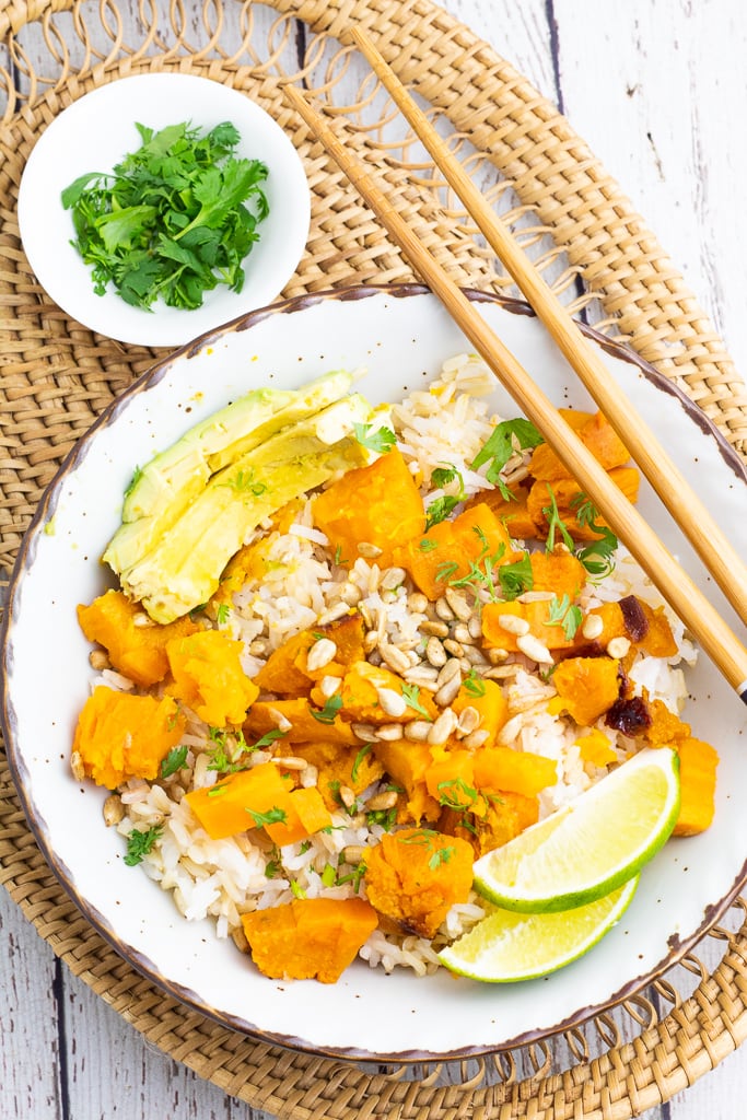 white bowl filled with rice, sweet potatoes, sesame seeds, cilantro, and sauce with chopsticks