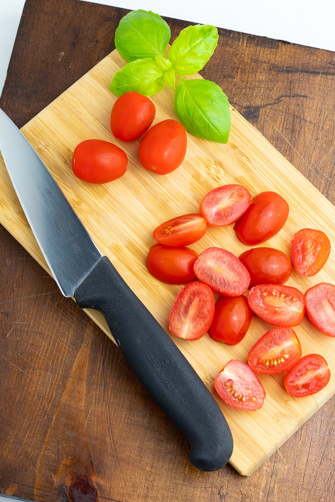 cutting board with cherry tomatoes slice in half with basil