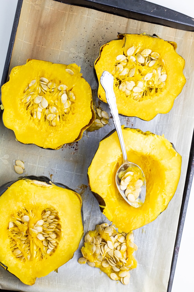 acorn squash cut in half on baking sheet with seeds being spooned out