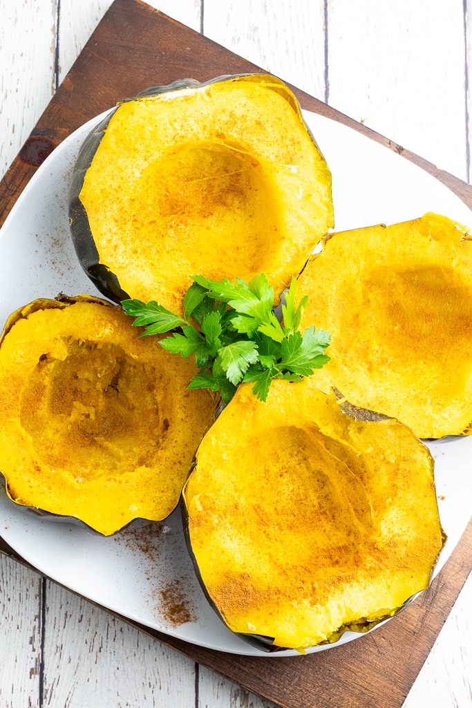 4 cooked acorn squash halves on plate with fresh parsley