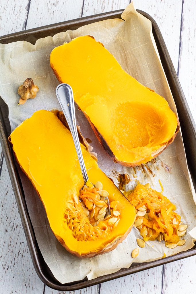 baking pan with 2 halves of a butternut squash with a spoon removing the seeds
