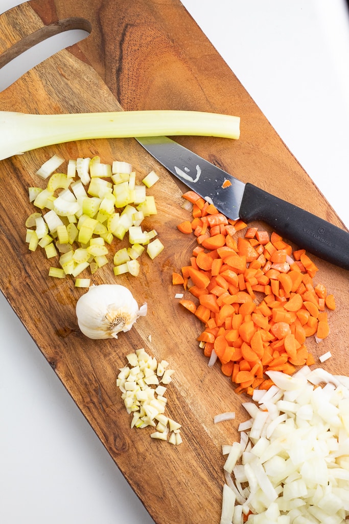 wooden cutting board with carrots, celery, onions, garlic