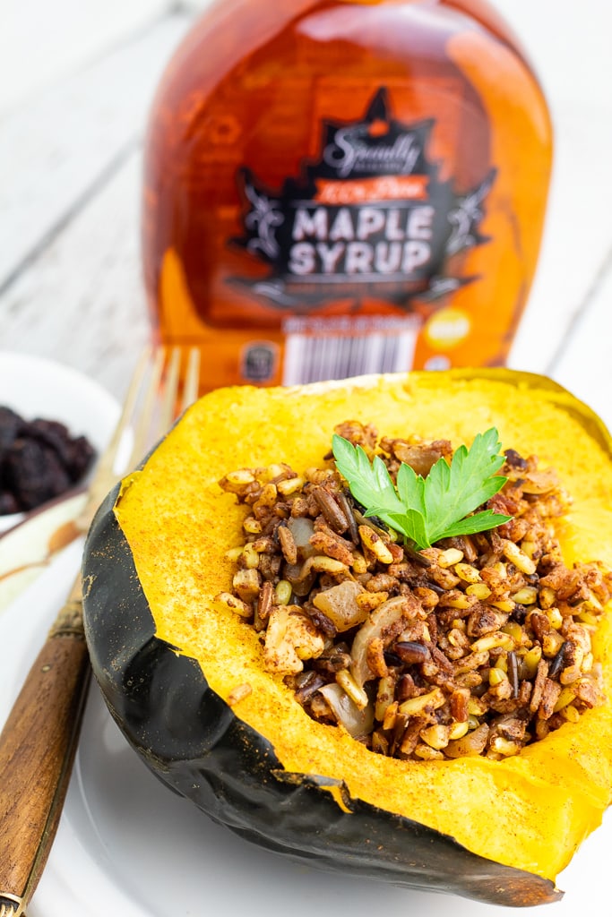acorn squash stuffed with wild rice, walnuts, and spices with bottle of maple syrup in background