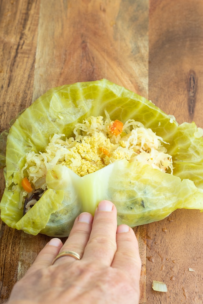 hand rolling up stuffed cabbage leaf on wooden board