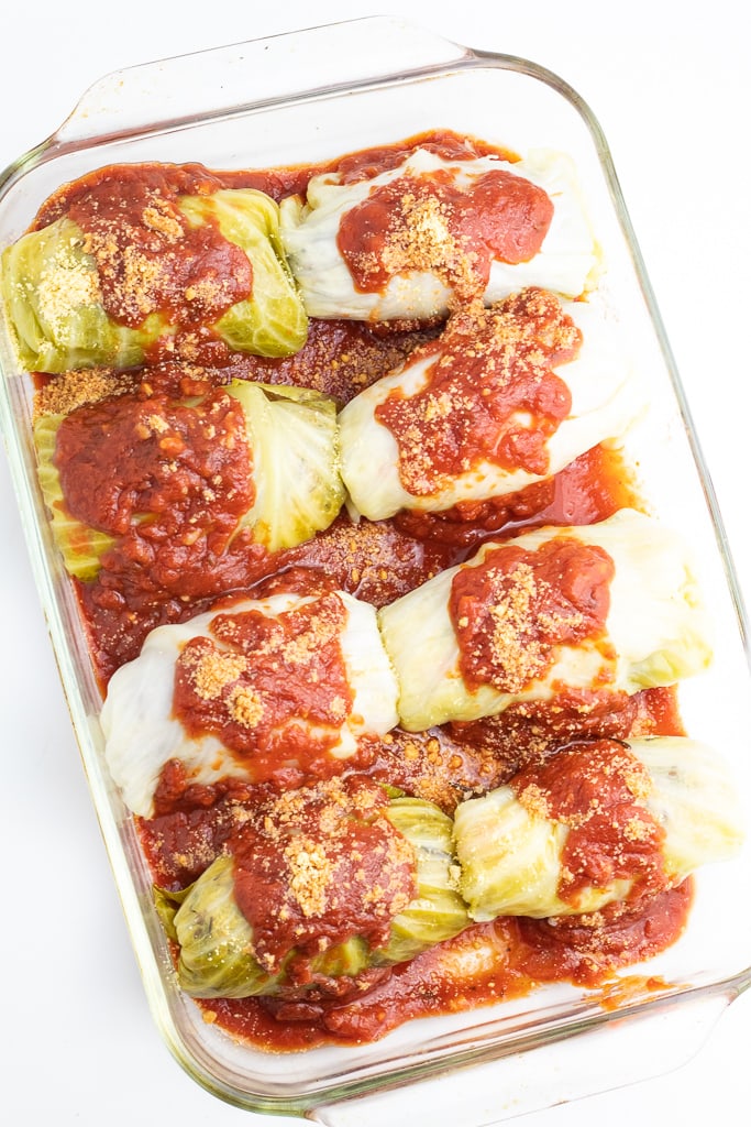 uncooked stuffed cabbage rolls in baking dish covered with marinara